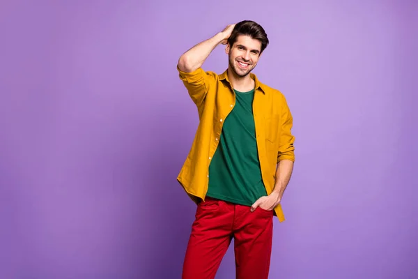 Foto de alegre hombre guapo atractivo positivo sonriendo con una sonrisa en pantalones rojos aislado violeta pastel color fondo peinándose el pelo — Foto de Stock