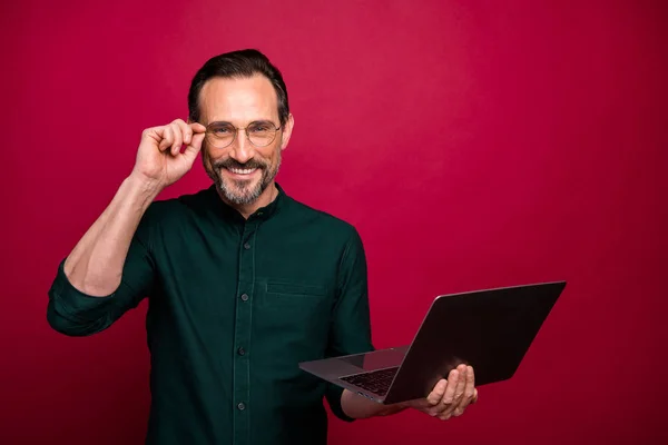 Foto da moda alegre positivo bonito homem segurando laptop sorrindo toothily perto do espaço vazio isolado cor vermelha vívida fundo — Fotografia de Stock