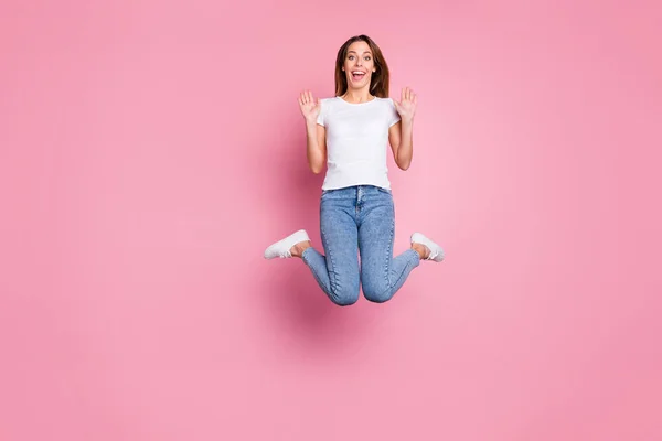 Photo of beautiful crazy lady jumping high enjoy summer sunny weekend days playful mood wear casual white t-shirt jeans sneakers isolated pink color background — 스톡 사진