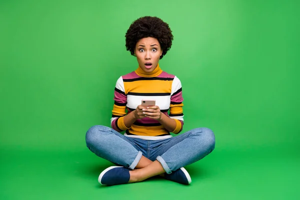 Foto em tamanho completo de menina surpreendida sentar pernas cruzadas dobrado uso celular blogging impressionado mídia social comentário repost grito omg desgaste roupas brilhantes isolado cor verde fundo — Fotografia de Stock