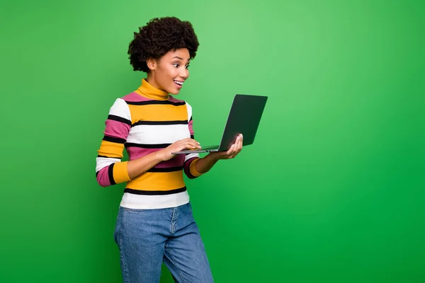 Foto profil dari wanita kulit gelap cantik wanita keriting memegang notebook membaca berita baik yang luar biasa gembira mengenakan jins bergaris-garis kasual terisolasi warna hijau latar belakang — Stok Foto