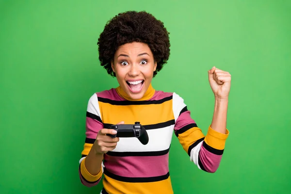 Photo of funny dark skin lady playing video games addicted gamer excited hold joystick hand celebrating winning raise fist wear casual striped sweater isolated green color background — 스톡 사진