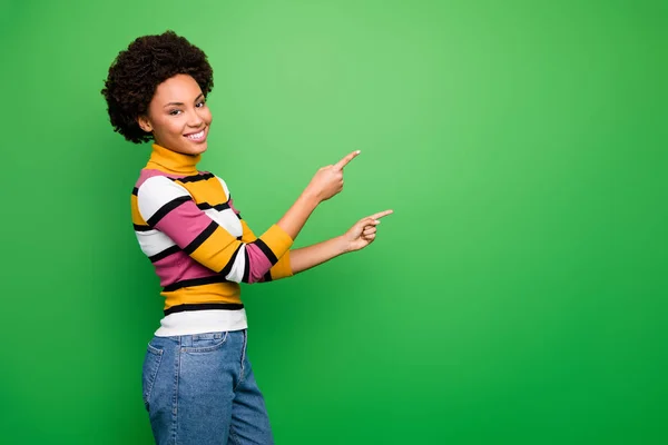 Profile photo of beautiful dark skin curly lady sales manager proposing good prices direct fingers empty space wear casual striped sweater jeans isolated green color background — Stockfoto