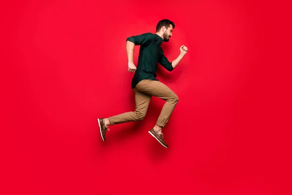 Полноразмерная фотография уверенного парня, прыгающего бегом, хочется быстро купить все весенние скидки, надеть коричневые брюки, изолированные на ярком цветовом фоне — стоковое фото