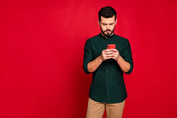 Portrait of concentrated guy use his smartphone solve work problems on social network wear casual style brown pants trousers isolated over red color background — 스톡 사진