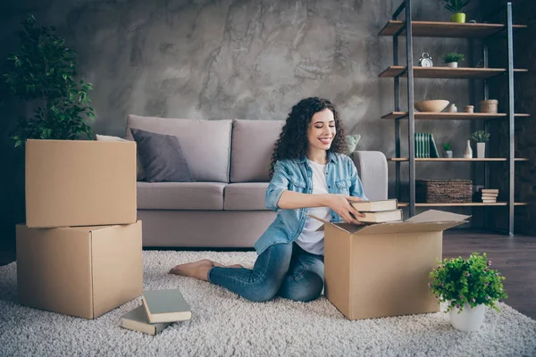 Niza atractiva encantadora alegre alegre chica de pelo ondulado sentado en la alfombra del piso de apertura desenvolver el desembalaje de sus propias cosas en el estilo industrial loft moderna sala de estar interior — Foto de Stock