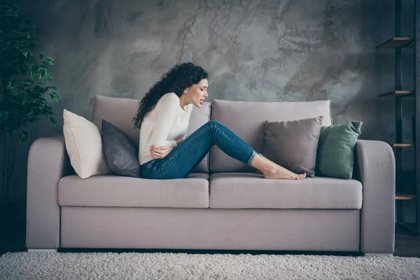 Perfil vista lateral de su atractiva deprimida niña de pelo ondulado poco saludable sentada en diván que sufre de problemas de vientre médico en el loft moderno estilo industrial interior sala de estar interior — Foto de Stock