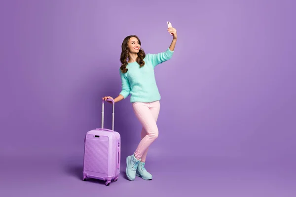 Full body profil zdjęcie dość wesoły lady spacer lotnisko rejestracja toczenia walizki podejmowania blog selfie nosić puszyste pastelowy sweter różowe spodnie buty odizolowane fioletowy kolor tła — Zdjęcie stockowe