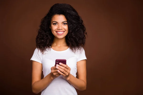 Πορτρέτο της γοητευτικής θετική afro american κορίτσι χρησιμοποιούν το κινητό τηλέφωνο απολαύσετε blogging λάτρης του κοινωνικού δικτύου φορούν μοντέρνα ρούχα απομονώνονται πάνω από καφέ φόντο χρώμα — Φωτογραφία Αρχείου