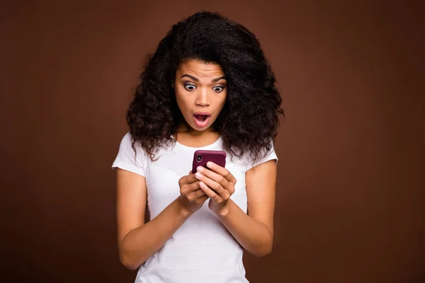 Portrait of crazy funky afro american girl use smart phone read social network information impressed scream wow omg wear casual style clothing isolated over brown color background — Stock Photo, Image