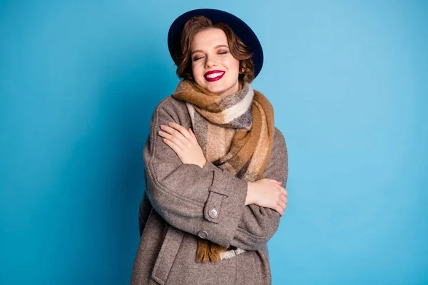 Φωτογραφία της όμορφης ταξιδιώτη κυρία κρατήστε τον εαυτό της ώμους μάτια κλειστά Απολαύστε ζεστασιά μαλακό ευχάριστο μαλλί φορούν κομψό casual μακρύ γκρι παλτό καπέλο καρό κασκόλ απομονωμένο μπλε χρώμα φόντο — Φωτογραφία Αρχείου