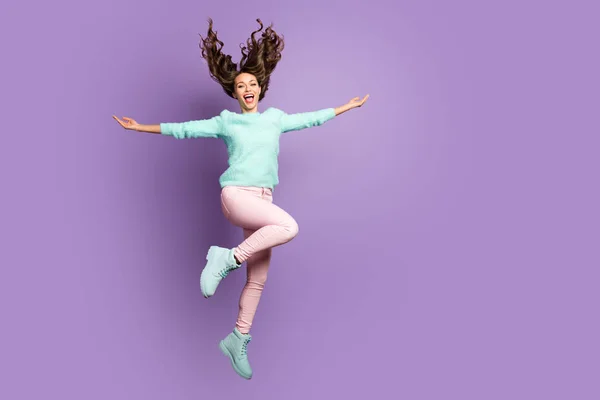 Full body foto van gekke grappig meisje springen hold handen genieten winnen blazen in haar kapsel slijtage roze broek zacht pastel pullover schoenen geïsoleerd over violet kleur achtergrond — Stockfoto