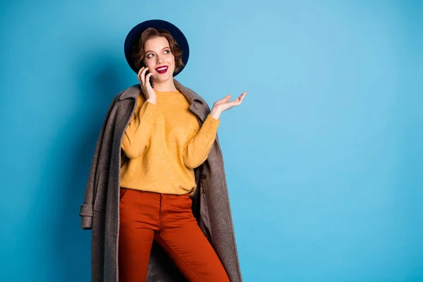 Φωτογραφία της όμορφης κυρίας με τα πόδια δρόμο ταξιδιώτη μιλώντας τηλέφωνο με τους φίλους λέει διεύθυνση για να πάει να φορέσει casual μακρύ γκρι παλτό πουλόβερ παντελόνι καπέλο παπούτσια απομονωμένο μπλε χρώμα φόντο — Φωτογραφία Αρχείου