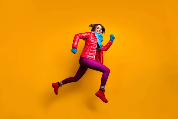 Teljes méretű profil fotó vicces hölgy ugrás fel nagy rohanó eladás vásárlás kopás alkalmi piros kabát kék sál kesztyű nadrág nadrág lábbeli elszigetelt sárga háttér — Stock Fotó