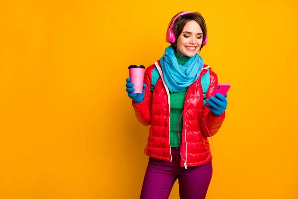 Photo of funny blogger lady walk street hold telephone listening earphones youth music drink hot coffee wear casual red coat blue scarf gloves pants isolated yellow color background — 图库照片