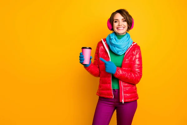 Photo of pretty lady hold paper mug takeout coffee directing finger on pink cup fresh americano wear casual red coat blue scarf gloves ear covers pants isolated yellow color background — 图库照片