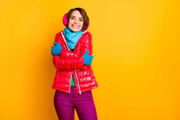 面白い陽気な女性の写真は、寒い天候の中で暖かいコートをお楽しみください抱擁彼女自身はカジュアルな短い赤いオーバーコートブルースカーフ手袋の耳フパンツ孤立黄色の色の背景を身に着けている — ストック写真