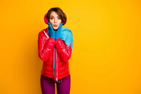 Photo of funny charming lady sending air kisses holding hands on cheekbones young millennial wear casual red overcoat blue gloves violet trousers isolated yellow color background