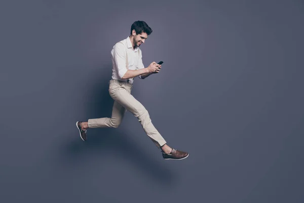 Full length photo of cheerful guy get message from girlfriend read sms from smartphone enjoy jump run date wear white shirt outfit isolated over grey color background — 图库照片