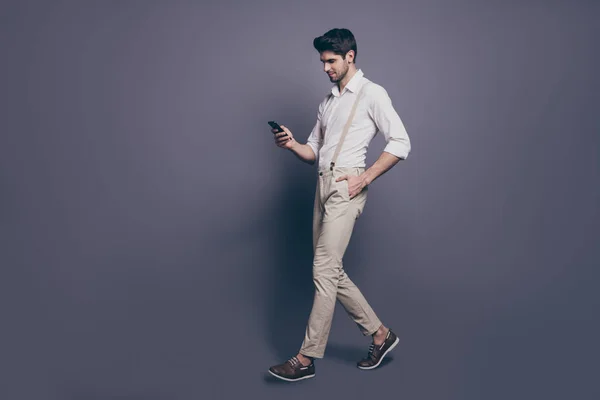 Volledige lengte profiel side photo of attractive luxury man go copyspace walk gebruik smartphone chat met blog volgers geheime bewonderaars dragen goed uitziende outfit geïsoleerde grijze kleur achtergrond — Stockfoto