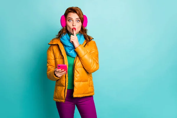 Dont speak. Photo of funny lady hold telephone finger on lips tell secret information ask to keep silence wear ear muffs yellow overcoat scarf pants isolated teal color background