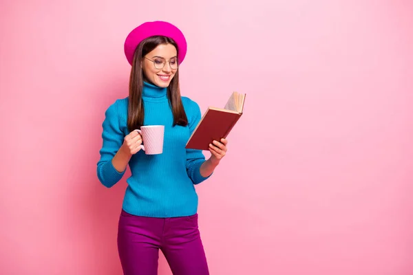 Retrato de chica alegre enfocado han fines de semana leer libro de texto celebrar taza de bebida caliente desgaste pantalones púrpura aislados sobre fondo de color pastel rosa — Foto de Stock