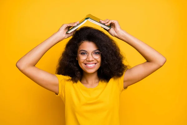 Primo piano ritratto di lei lei bella attraente bella funky comico allegro allegro allegro ragazza dai capelli ondulati ingannare tenendo libro sopra la testa isolato su brillante vivido brillare vibrante colore giallo sfondo — Foto Stock