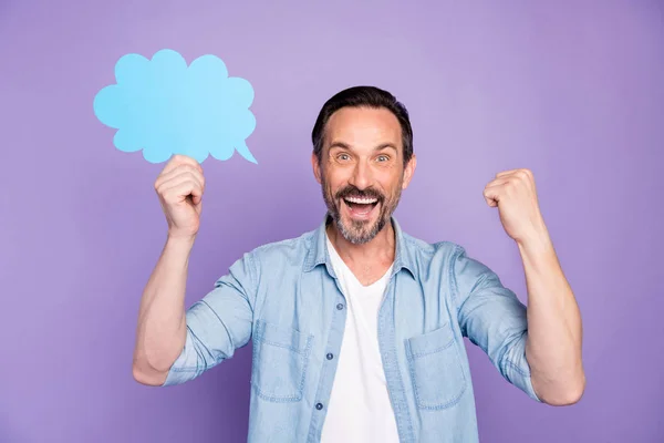 Portrait of delighted man hold paper card blue speech bubble think about his win raise fists scream yeah wear good looking outfit isolated over purple color background — Stok fotoğraf