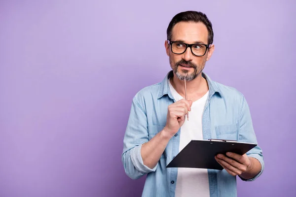 Portrait of interested man job worker hold clip board want write thoughts think touch pencil chin look copyspace wear casual style clothes isolated over purple color background — ストック写真