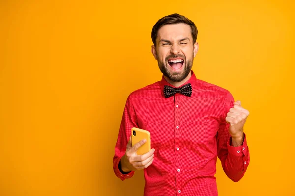 Photo of attractive guy hold telephone social network worker celebrating growth blog popularity formalwear look trendy red shirt bow tie isolated yellow color background — Stok fotoğraf