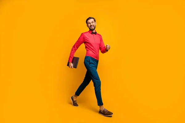 Full length profile photo of macho business man walk corporate meeting training carry laptop wear stylish red shirt bow tie blue pants shoes isolated yellow color background — Zdjęcie stockowe