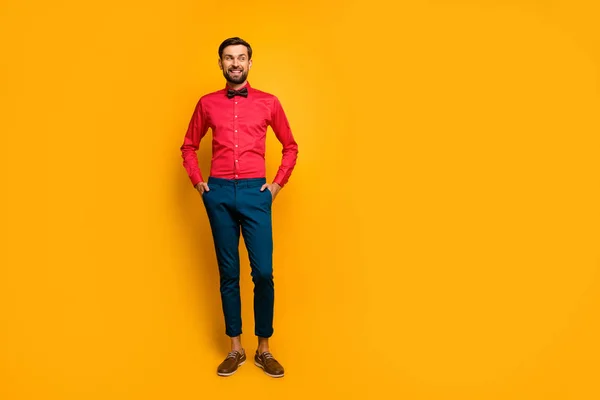 Full length photo of amazing macho man good mood friendly smiling look side empty space wear stylish red shirt with bow tie blue pants shoes isolated yellow color background — 스톡 사진