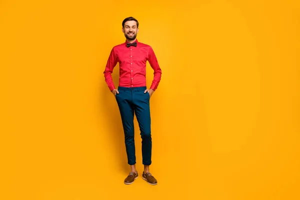 Plná délka fotografie úžasné macho muž stojící dobré nálady přátelský zářící úsměv oblečení stylové červené košile s motýlkem modré kalhoty boty izolované žluté pozadí — Stock fotografie