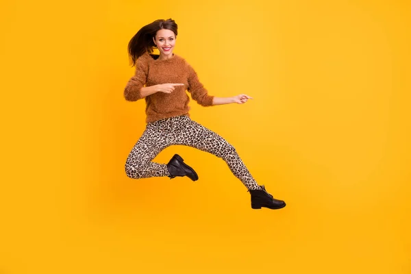 Full längd foto av ganska rolig dam hoppa högt indikerar fingrar tomt utrymme råda sista säsongen försäljning bära fluffig pullover leopard byxor skor isolerad gul färg bakgrund — Stockfoto