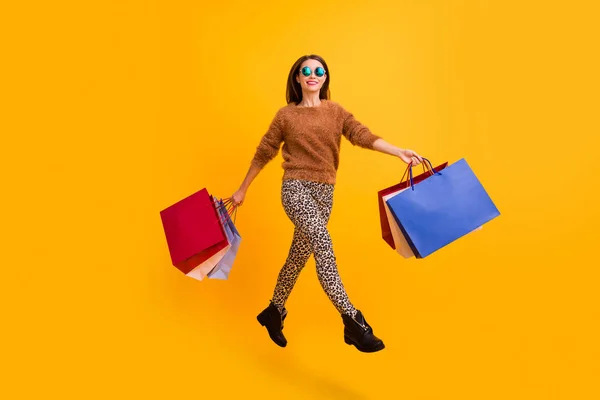 Full body profile photo of pretty funny lady jumping high carry many packs excited shopper wear fluffy sweater leopard trousers footwear isolated yellow color background — Stock Photo, Image