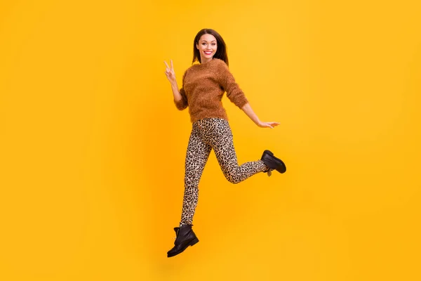 Foto de perfil de corpo inteiro de senhora funky pulando alto bom humor juventude olhar andar rua mostrar v-sinal símbolo amigos desgaste fofo camisola leopardo calças botas isolado cor amarela fundo — Fotografia de Stock