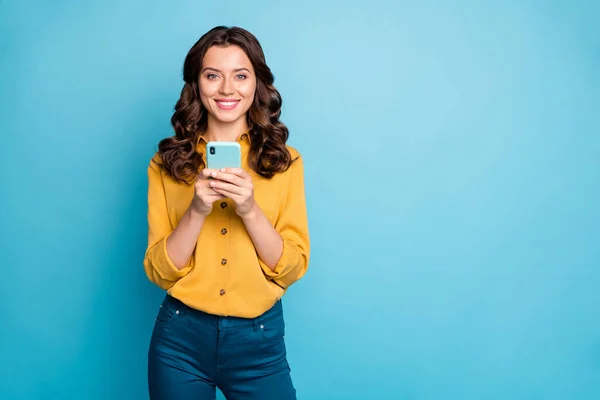 Photo of pretty freelancer lady holding telephone hands reading new positive comments instagram blog post wear yellow shirt trousers isolated blue color background — 스톡 사진