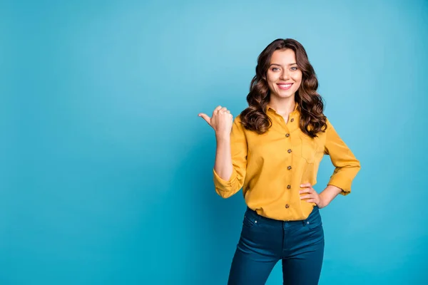 Photo of lovely business manager lady indicating thumb finger empty space advising new product low price wear yellow shirt pants isolated blue color background — 스톡 사진