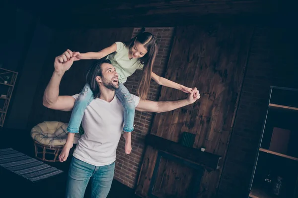 Foto av lilla funky vacker dam sitter på axlarna upphetsad stilig pappa bära dotter spelar spel hålla händerna glada gott humör glädje hus rum inomhus — Stockfoto