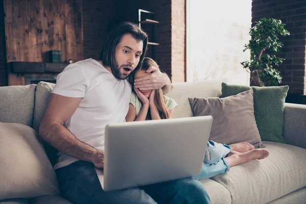 Ne nézz oda! Fénykép a kis csinos hölgy ül kényelmes kanapé jóképű apa használja notebook nézni ijesztő film fogja a kezét a szemét nyitott száj horror ház szoba beltéri — Stock Fotó