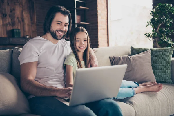 Fénykép a kis csinos hölgy ül kényelmes kanapé jóképű apa néz kedvenc karácsonyi film beszél skype rokonok segítségével notebook jó hangulatú ház szoba beltérben — Stock Fotó