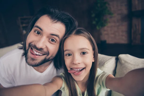 Primeros planos foto de la pequeña señora divertida su apuesto joven papá sentarse cómodo sofá haciendo tomar selfies pegando lengua por la boca pasar fin de semana habitación de la casa en el interior — Foto de Stock