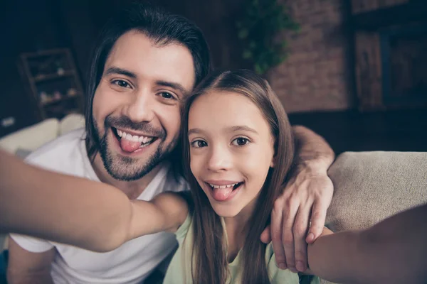 Güzel, küçük, komik bir bayanın fotoğrafı. Yakışıklı, genç babası rahat bir kanepeye oturup selfie çekiyor. Dilini ağzından çıkarıyor. — Stok fotoğraf