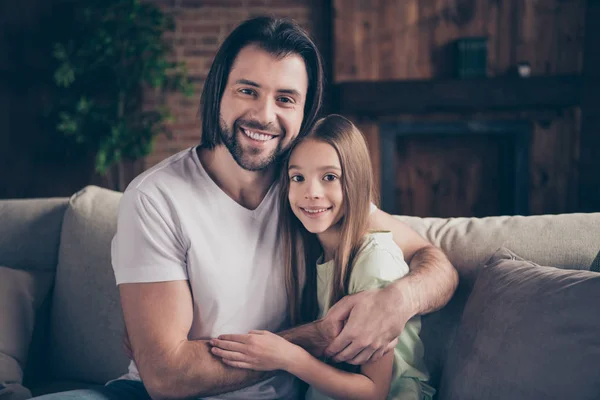 Photo of beautiful pretty little lady and her handsome daddy sitting comfy sofa hugging together toothy adorable smile spending weekend time homey house room indoors — Stock Photo, Image