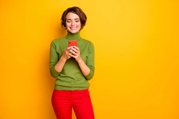 ポジティブな陽気な女の子の肖像画を使用してスマートフォンは、オンラインソーシャルネットワーク通信を持っている読み取りニュースは明るい色の背景に孤立スタイリッシュな赤緑の衣装を身に着けている — ストック写真