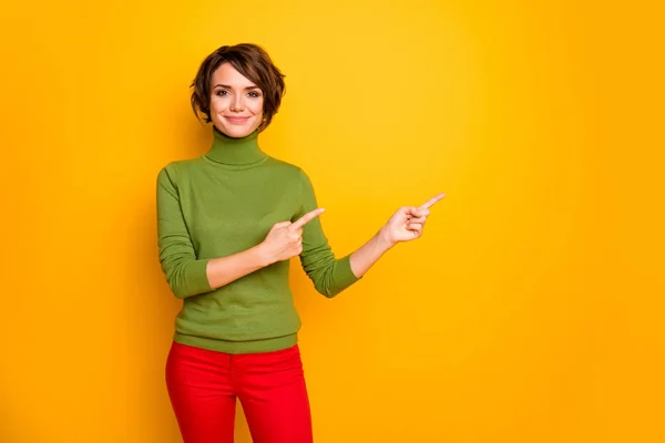 Venta. Foto de atractiva señora divertida indican dedos espacio vacío aconsejando viernes negro precios bajos desgaste casual cuello alto verde pantalones rojos aislados color amarillo fondo —  Fotos de Stock