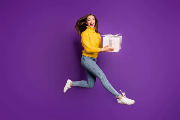 Full length body size profile side photo of cheerful positive cute pretty girl holding wrapped box running jumping up for sale isolated vivid purple color background — Stock Photo, Image