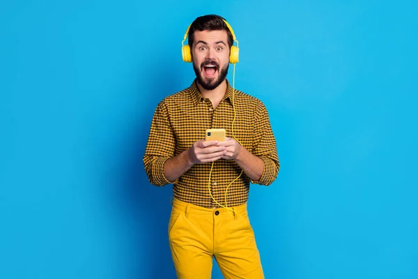 Omg my favorite song. Astonished excited man use smartphone search stereo volume melody scream listen music wear headset checkered trousers style stylish trendy isolated blue color background — 스톡 사진