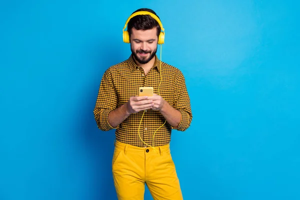 Portrait of positive cheerful man enjoy listen music stereo from his smartphone wear total yellow bright headset plaid trousers isolated over blue color background — 스톡 사진