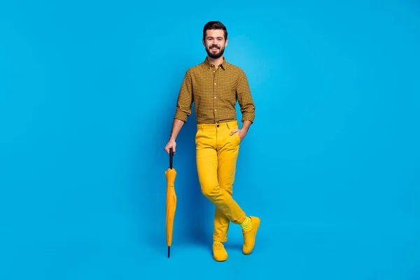 Volledige lengte foto van openhartige imposante man rust ontspannen hebben levendige bescherming schild regenstorm parasol dragen moderne kleding schoenen geïsoleerd over blauwe kleur achtergrond — Stockfoto